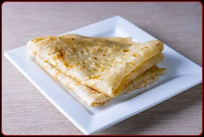 2 Wheat chapati folded and placed on a white plate.